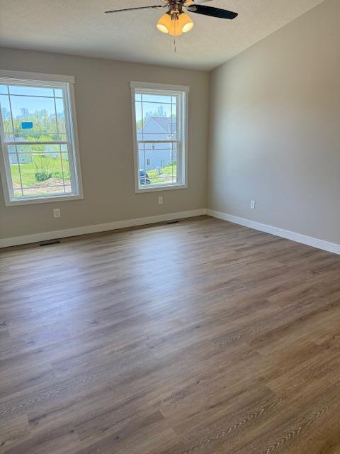unfurnished room featuring baseboards, a ceiling fan, dark wood finished floors, and a wealth of natural light