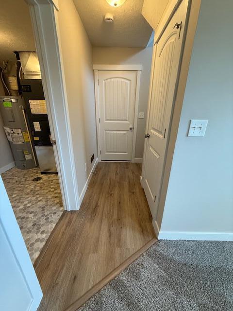 corridor featuring baseboards, wood finished floors, and water heater