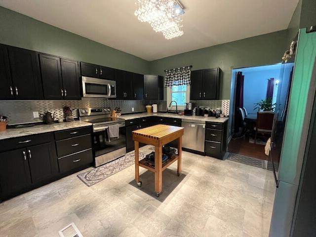 kitchen with a sink, light countertops, dark cabinets, stainless steel appliances, and backsplash
