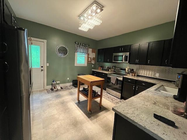 kitchen featuring backsplash, appliances with stainless steel finishes, a sink, a notable chandelier, and dark cabinetry