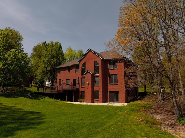back of property featuring brick siding, a lawn, and a wooden deck