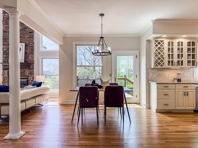 dining area featuring crown molding, a chandelier, baseboards, decorative columns, and wood finished floors