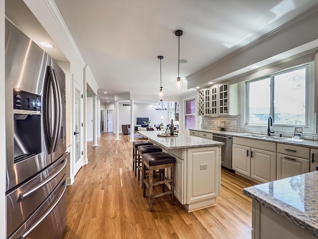 kitchen with light wood-style floors, tasteful backsplash, a sink, glass insert cabinets, and stainless steel appliances