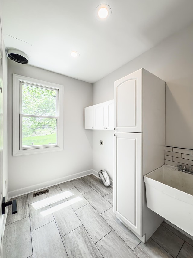 clothes washing area with hookup for an electric dryer, visible vents, cabinet space, a sink, and baseboards