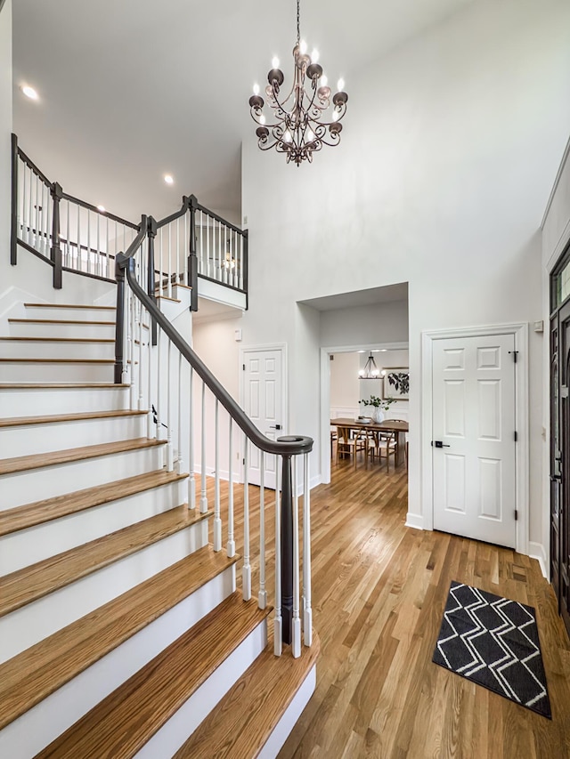 entrance foyer with a high ceiling, a notable chandelier, stairs, baseboards, and wood finished floors