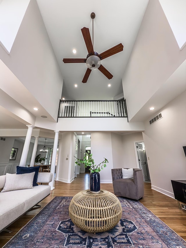 living room with a high ceiling, a ceiling fan, decorative columns, wood finished floors, and visible vents