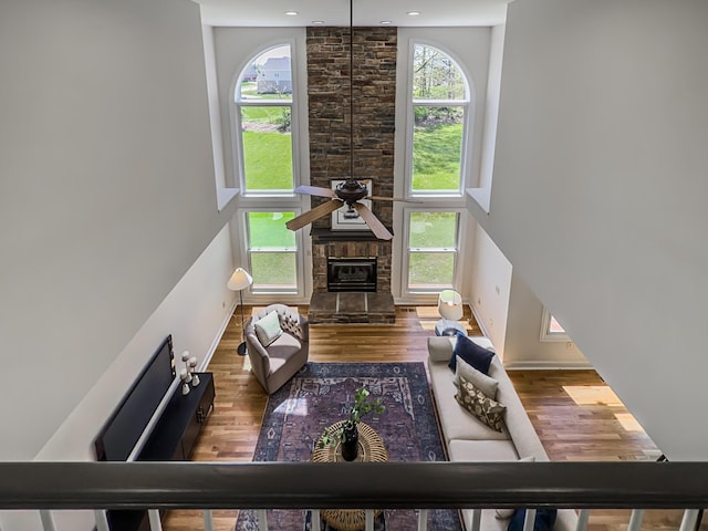 living area with baseboards, a ceiling fan, a stone fireplace, and wood finished floors