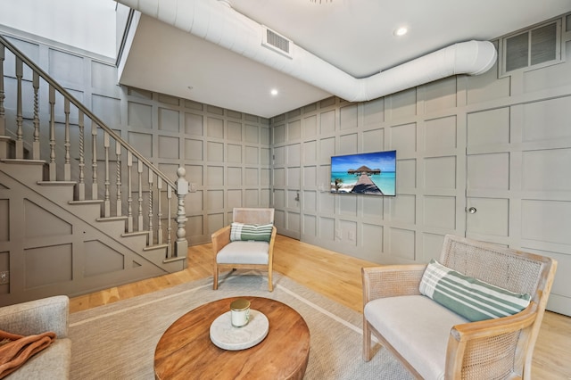 sitting room with wood finished floors, visible vents, a decorative wall, and stairway