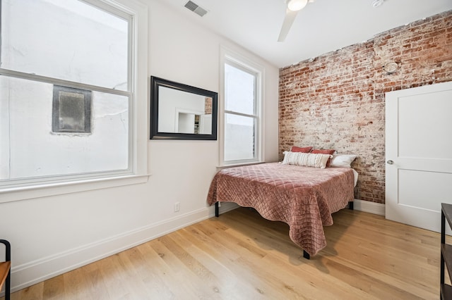 bedroom featuring multiple windows, brick wall, baseboards, and wood finished floors