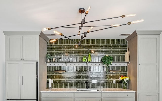 bar featuring a notable chandelier, decorative backsplash, paneled refrigerator, and a sink