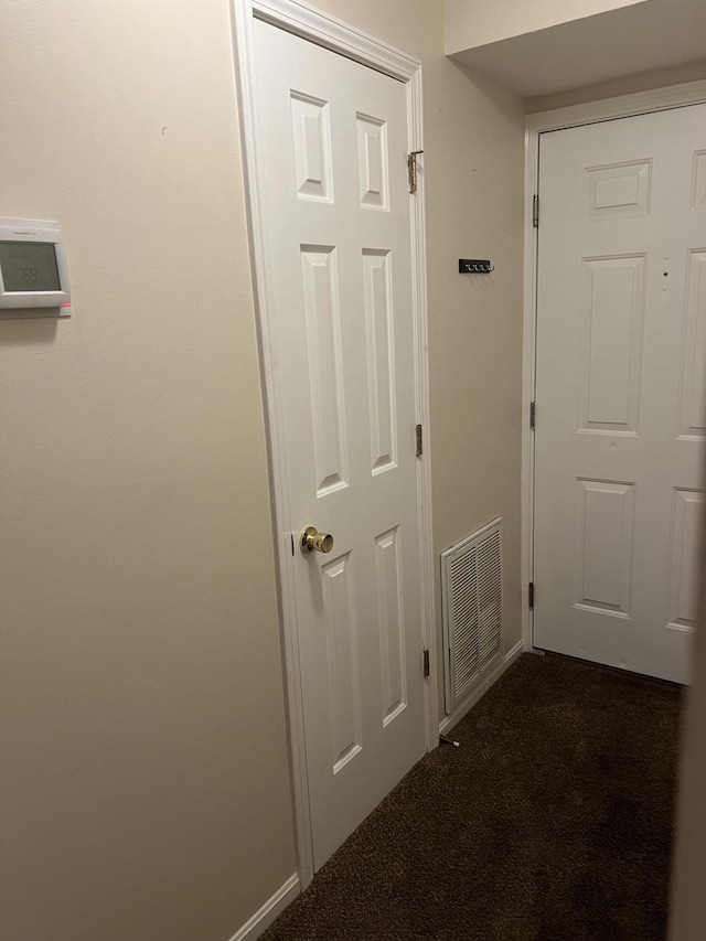 hallway featuring visible vents, baseboards, and dark colored carpet