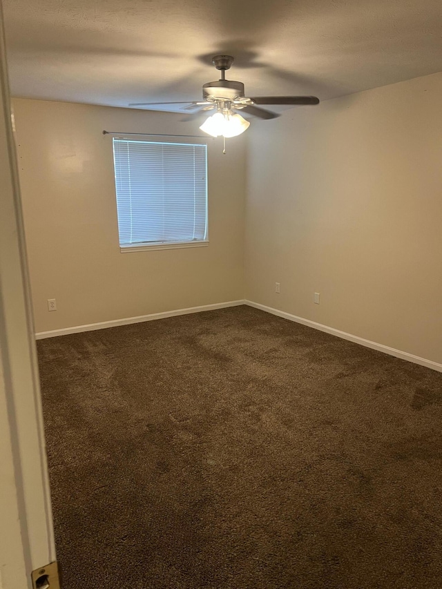 empty room featuring ceiling fan, baseboards, and dark colored carpet