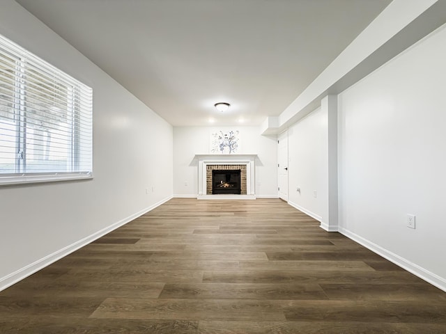 unfurnished living room with baseboards, a brick fireplace, and wood finished floors