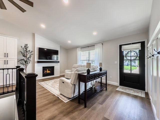 living area with a large fireplace, vaulted ceiling, dark wood-style flooring, and a wealth of natural light
