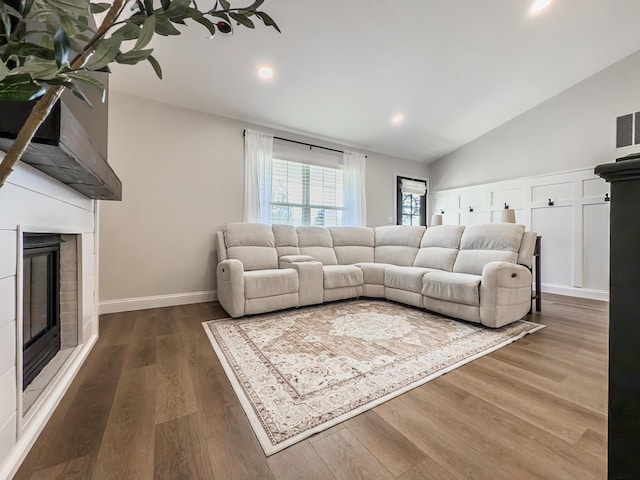living room with a glass covered fireplace, wood finished floors, lofted ceiling, baseboards, and recessed lighting