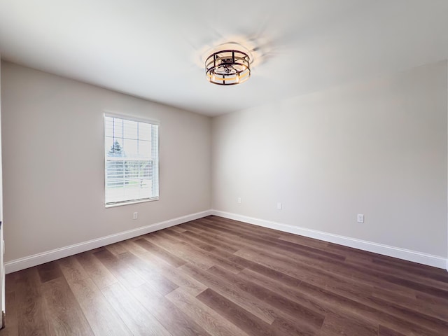 spare room featuring baseboards, an inviting chandelier, and dark wood-type flooring