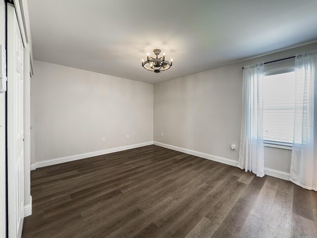 unfurnished bedroom with baseboards, a notable chandelier, and dark wood-style floors