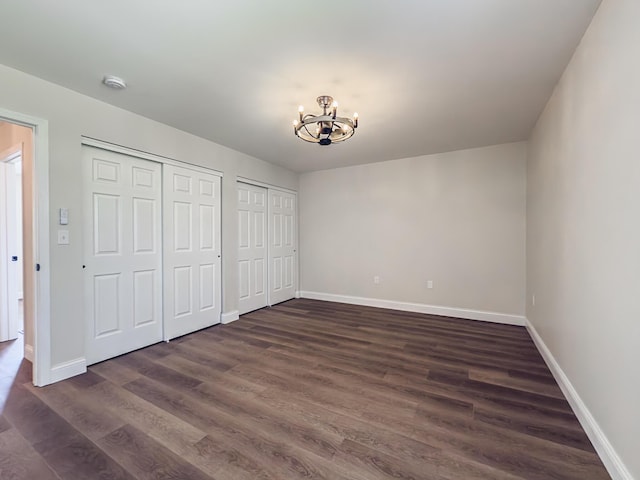 unfurnished bedroom with an inviting chandelier, baseboards, dark wood-style flooring, and two closets