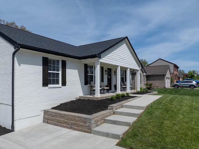 view of front of house featuring a porch, brick siding, roof with shingles, and a front yard