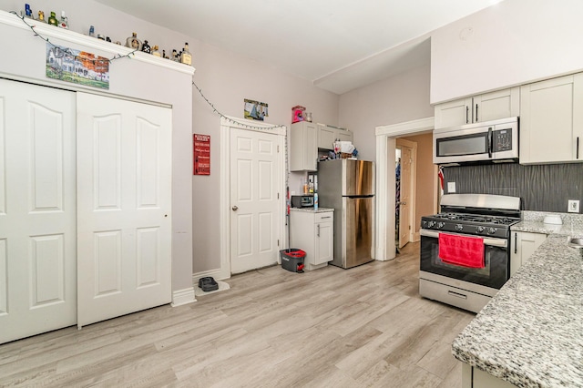kitchen with appliances with stainless steel finishes, light wood finished floors, and light stone counters