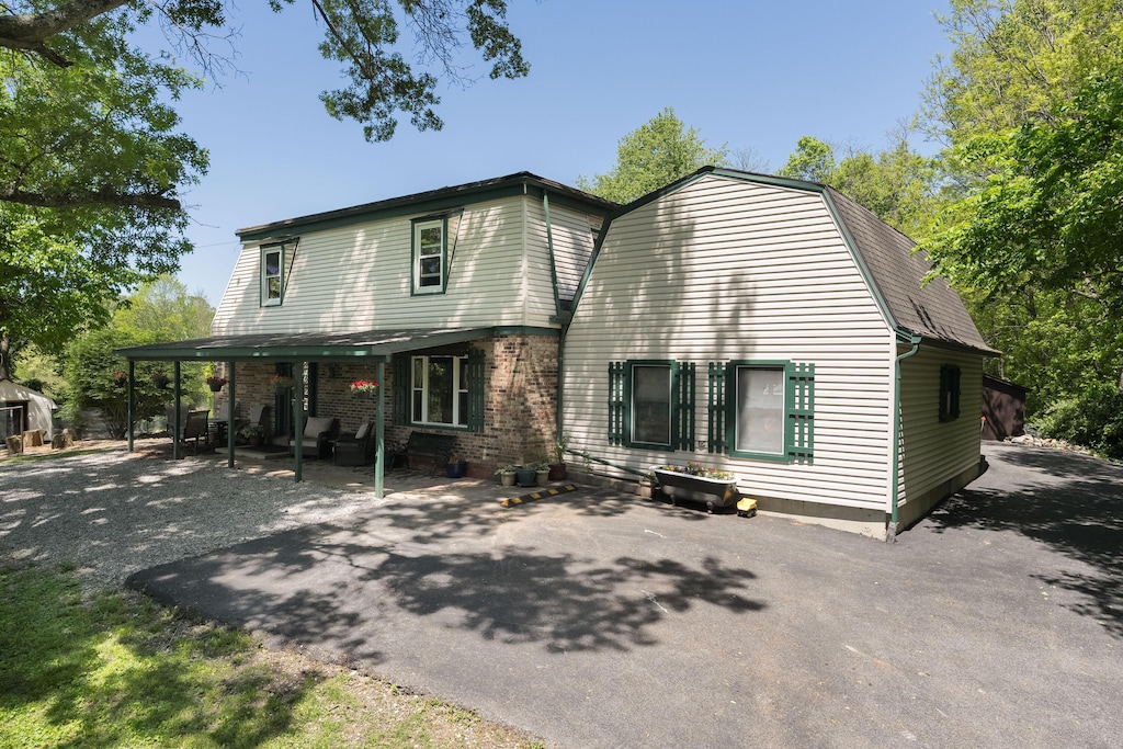 rear view of house with a gambrel roof, a patio area, and brick siding
