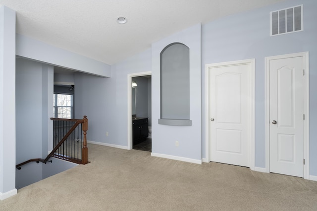 carpeted empty room with baseboards, visible vents, and lofted ceiling