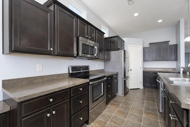 kitchen featuring stone finish floor, appliances with stainless steel finishes, dark countertops, a sink, and recessed lighting