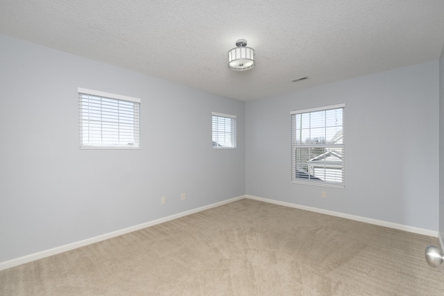 empty room featuring a textured ceiling, baseboards, visible vents, and light carpet