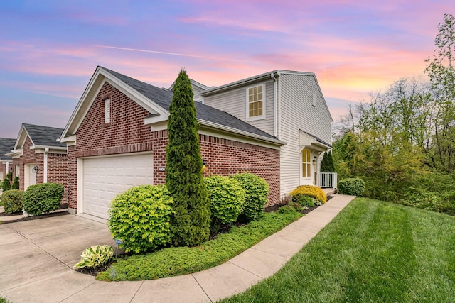 view of side of property with brick siding, an attached garage, a lawn, and driveway