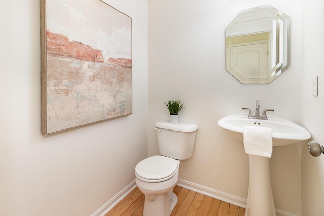 half bath featuring a sink, baseboards, toilet, and wood finished floors