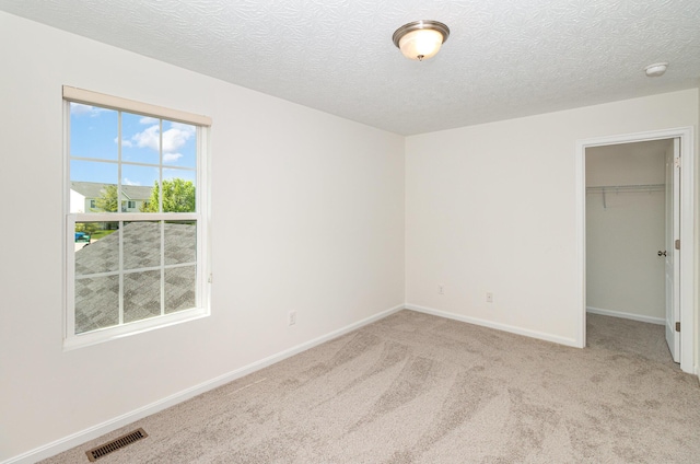 unfurnished bedroom with carpet flooring, a textured ceiling, visible vents, and a walk in closet