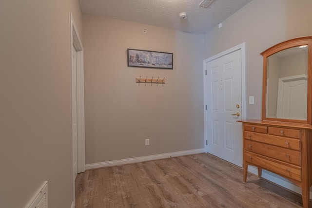 foyer with light wood finished floors, baseboards, and a textured ceiling