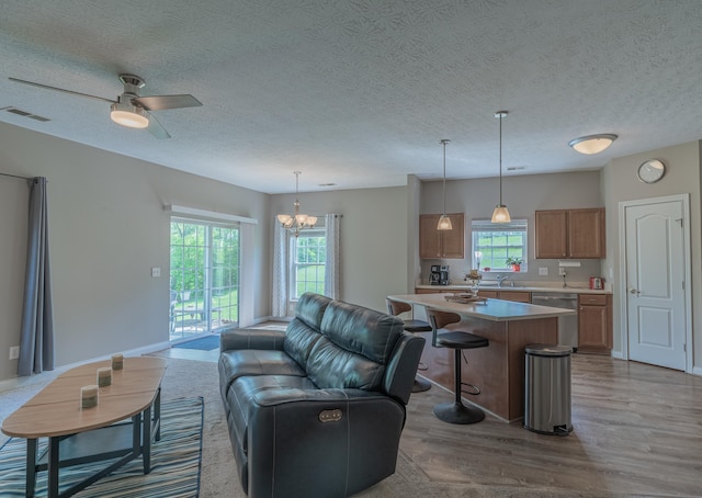 living area with wood finished floors, plenty of natural light, a chandelier, ceiling fan, and a textured ceiling