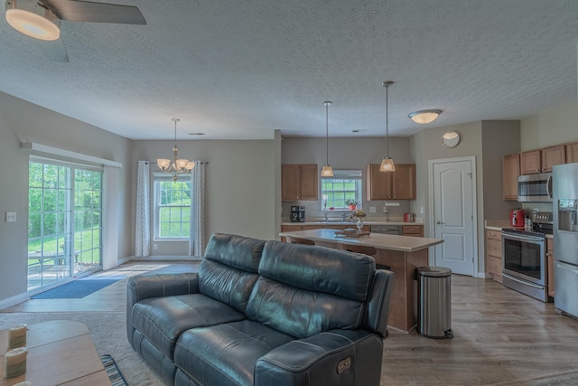 living area featuring a chandelier, light wood-style flooring, ceiling fan, a textured ceiling, and baseboards