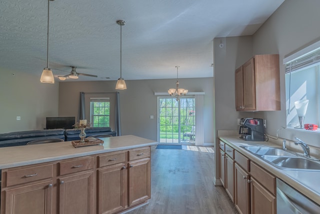 kitchen with a sink, dishwasher, a chandelier, wood finished floors, and light countertops