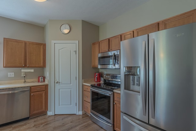 kitchen with stainless steel appliances, light wood-style floors, light countertops, and brown cabinets
