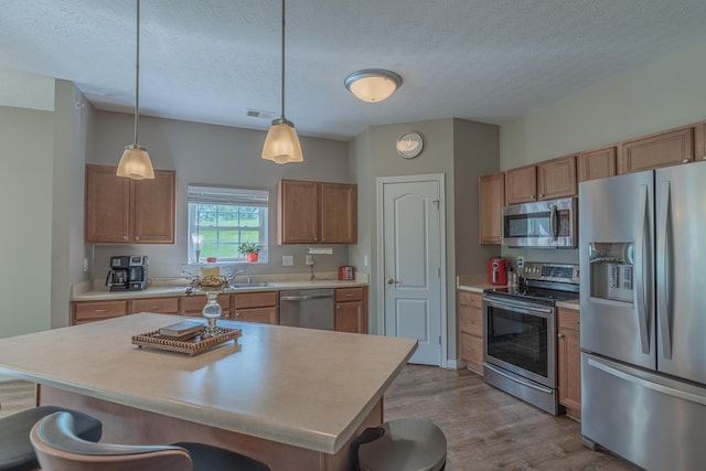 kitchen featuring stainless steel appliances, a breakfast bar area, wood finished floors, light countertops, and decorative light fixtures