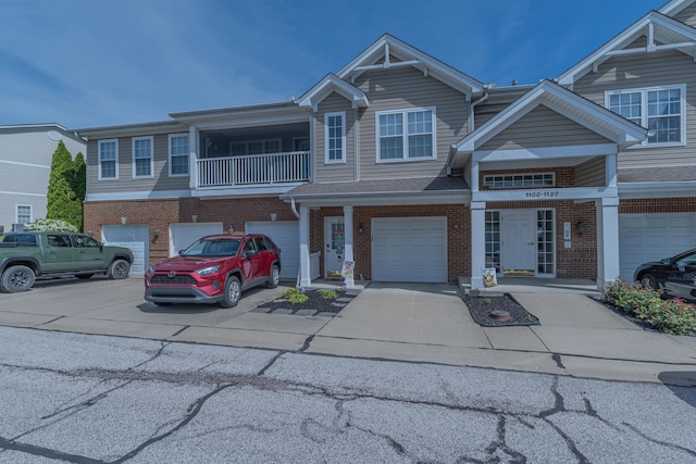 townhome / multi-family property with driveway, an attached garage, brick siding, and a balcony