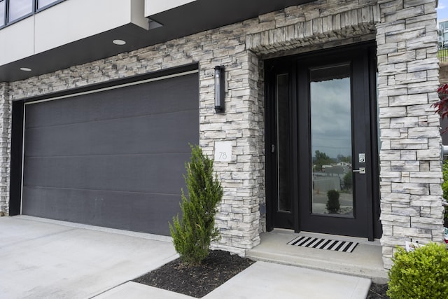 view of exterior entry with stone siding and a garage