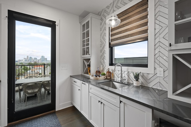 bar featuring decorative backsplash, hanging light fixtures, a sink, a city view, and dark wood-style floors