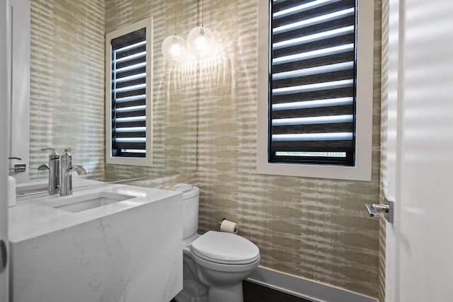 half bath featuring a sink, toilet, and wallpapered walls