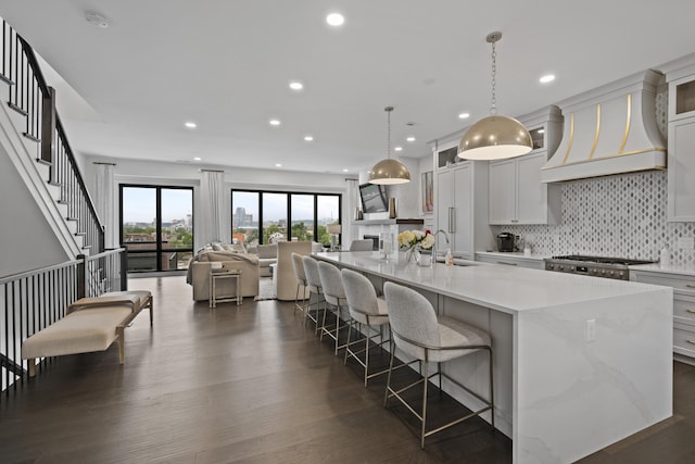 kitchen featuring backsplash, a kitchen bar, a large island, a sink, and custom range hood