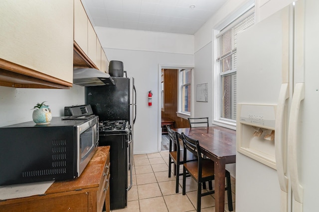 910 Hamlet St, Newport, KY 41071 - kitchen with light tile patterned flooring, white refrigerator with ice dispenser, gas range oven, stainless steel microwave, and under cabinet range hood
