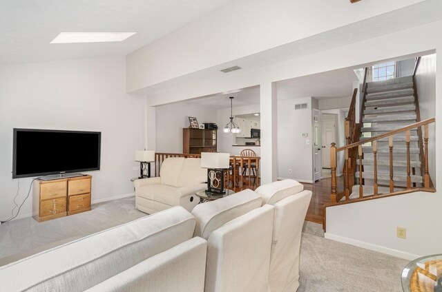 carpeted living room featuring stairs, baseboards, visible vents, and vaulted ceiling with skylight