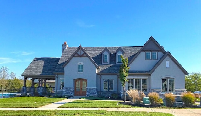 view of front of house featuring a front lawn, stucco siding, french doors, and stone siding