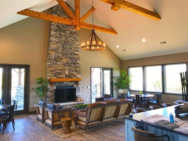 living area featuring wood finished floors, beamed ceiling, a stone fireplace, high vaulted ceiling, and a chandelier