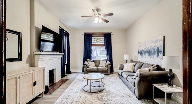 living area with light wood-style floors, baseboards, a ceiling fan, and a brick fireplace