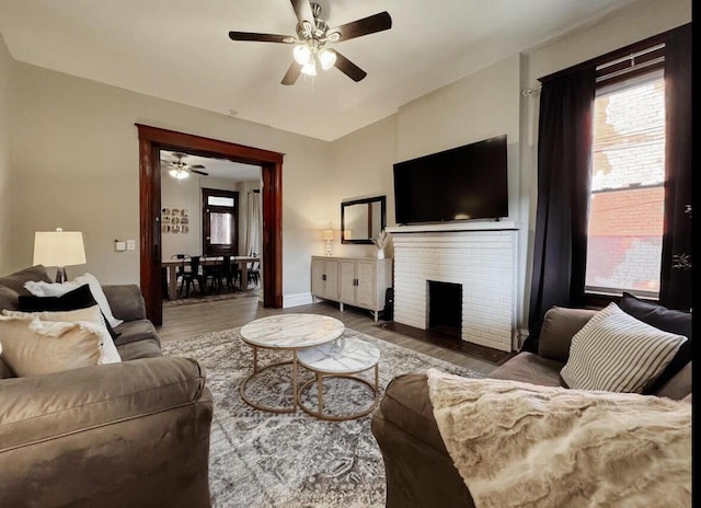 living area featuring baseboards, ceiling fan, wood finished floors, and a fireplace