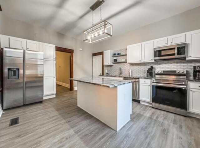 kitchen with backsplash, white cabinetry, appliances with stainless steel finishes, and light wood finished floors