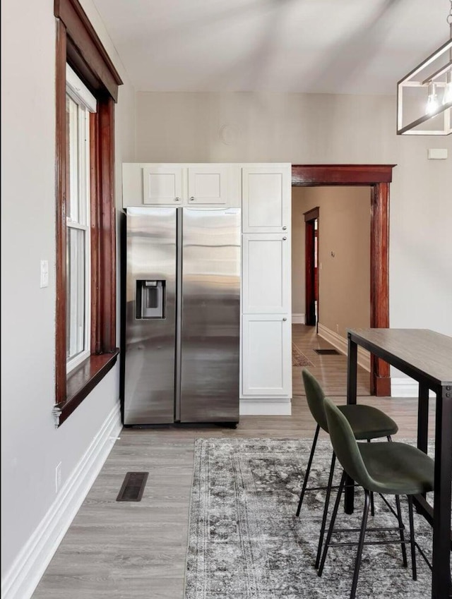 kitchen featuring baseboards, white cabinets, stainless steel refrigerator with ice dispenser, and visible vents